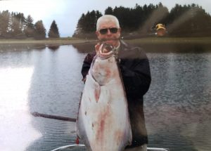 Unusual Fish and Game Meat. Ed Edwards holding fishing pole in mouth with large fish on it